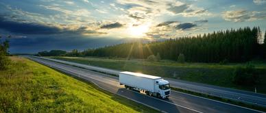 White truck driving on the highway in the countryside in the rays of the sunset with dramatic clouds