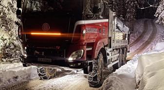 A red and white TATRA truck navigates a wintry road, flanked by a dense forest under a dark night sky.