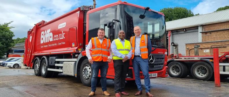 Three men in safety vests standing with red Biffa refuse truck