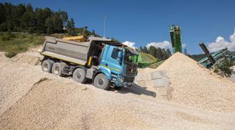 A blue truck with a gray dump bed travels down a gravel hill in a quarry.