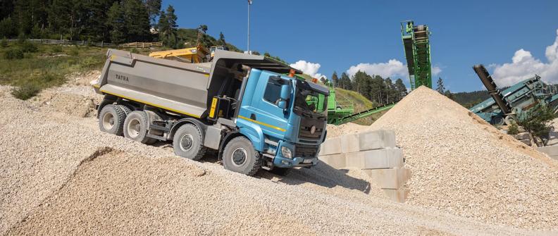 A blue truck with a gray dump bed travels down a gravel hill in a quarry.