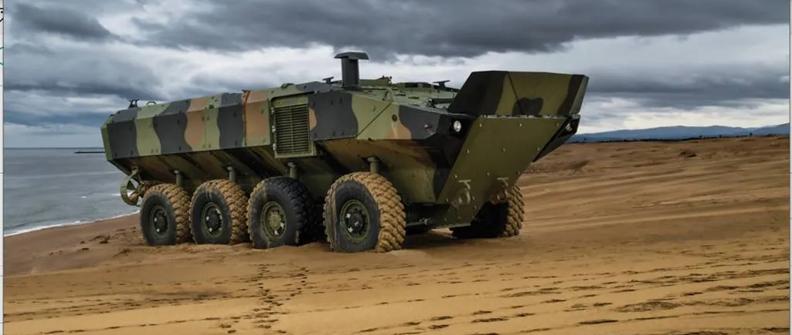 An IDV amphibious combat vehicle climbs up on the sand next to a body of water.