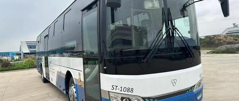 A blue and white bus sits parked in a dirt lot.