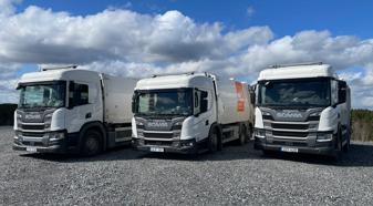 Three Scania refuse trucks are parked in a gravel lot.