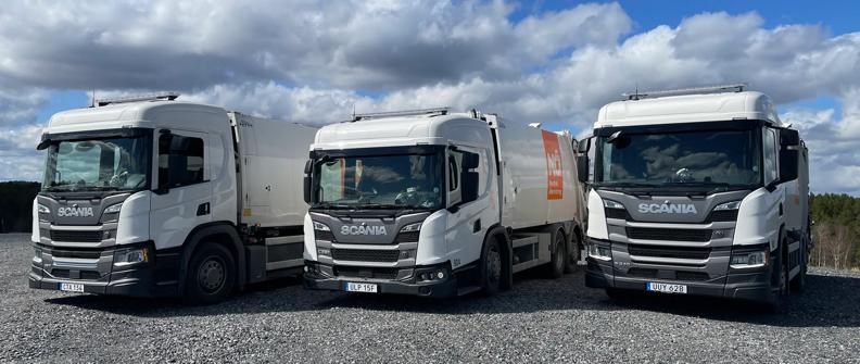 Three Scania refuse trucks are parked in a gravel lot.