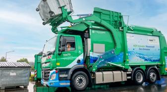 Green zero emission refuse truck lifting a trash receptacle