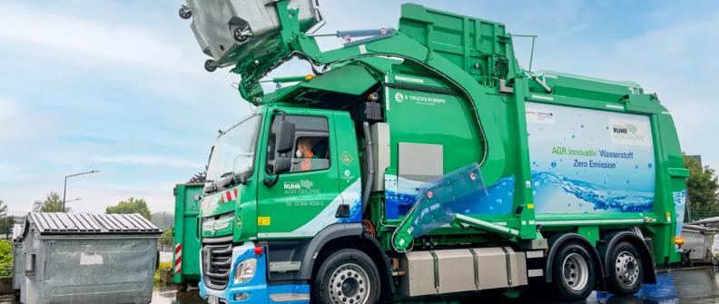 Green zero emission refuse truck lifting a trash receptacle