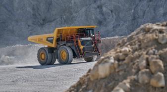 A yellow Volvo mining truck drives through a quarry.