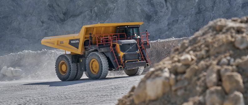 A yellow Volvo mining truck drives through a quarry.