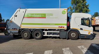 A white refuse vehicle with green and orange stripes sits in a parking lot.