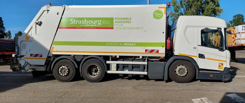 A white refuse vehicle with green and orange stripes sits in a parking lot.
