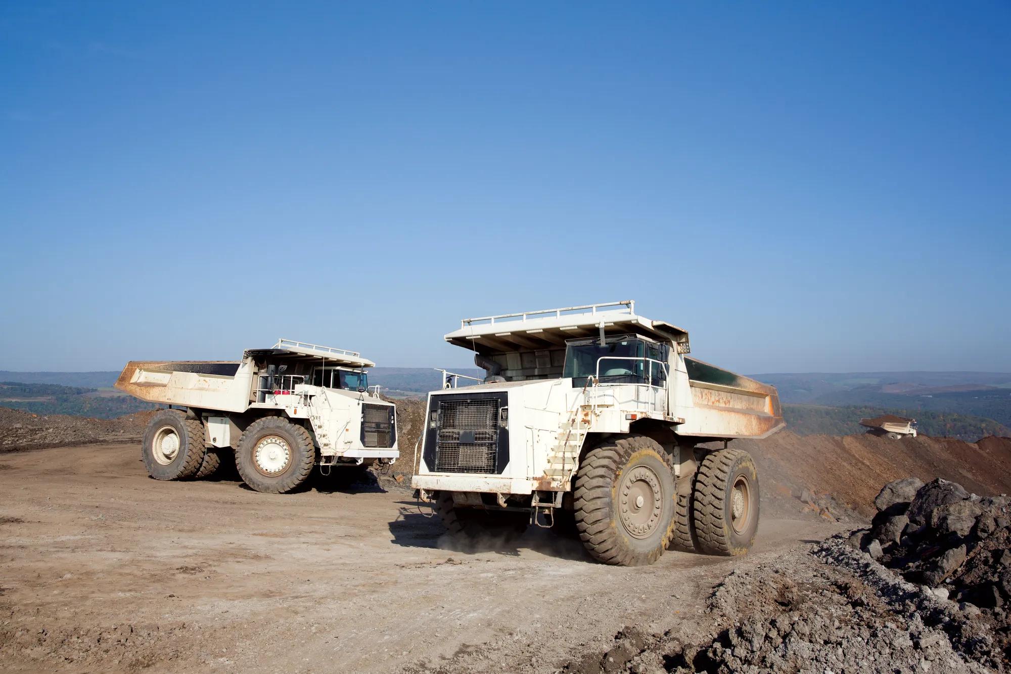 Foto de dos camiones de minería blancos en una obra.