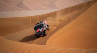 A gray, red and black Dakar Rally truck travels down a sand dune during the Dakar Rally in Saudi Arabia.