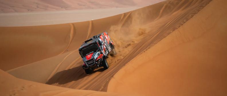 A gray, red and black Dakar Rally truck travels down a sand dune during the Dakar Rally in Saudi Arabia.