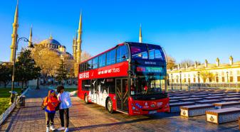 An image of a red double decker bus advertising Hop on Hop Off tours in front of the main mosque in Istanbul.