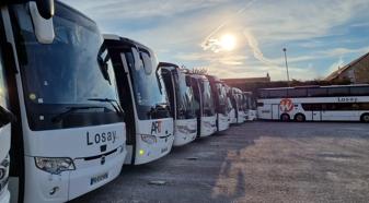 An image of a line of white coach buses in the setting sun.