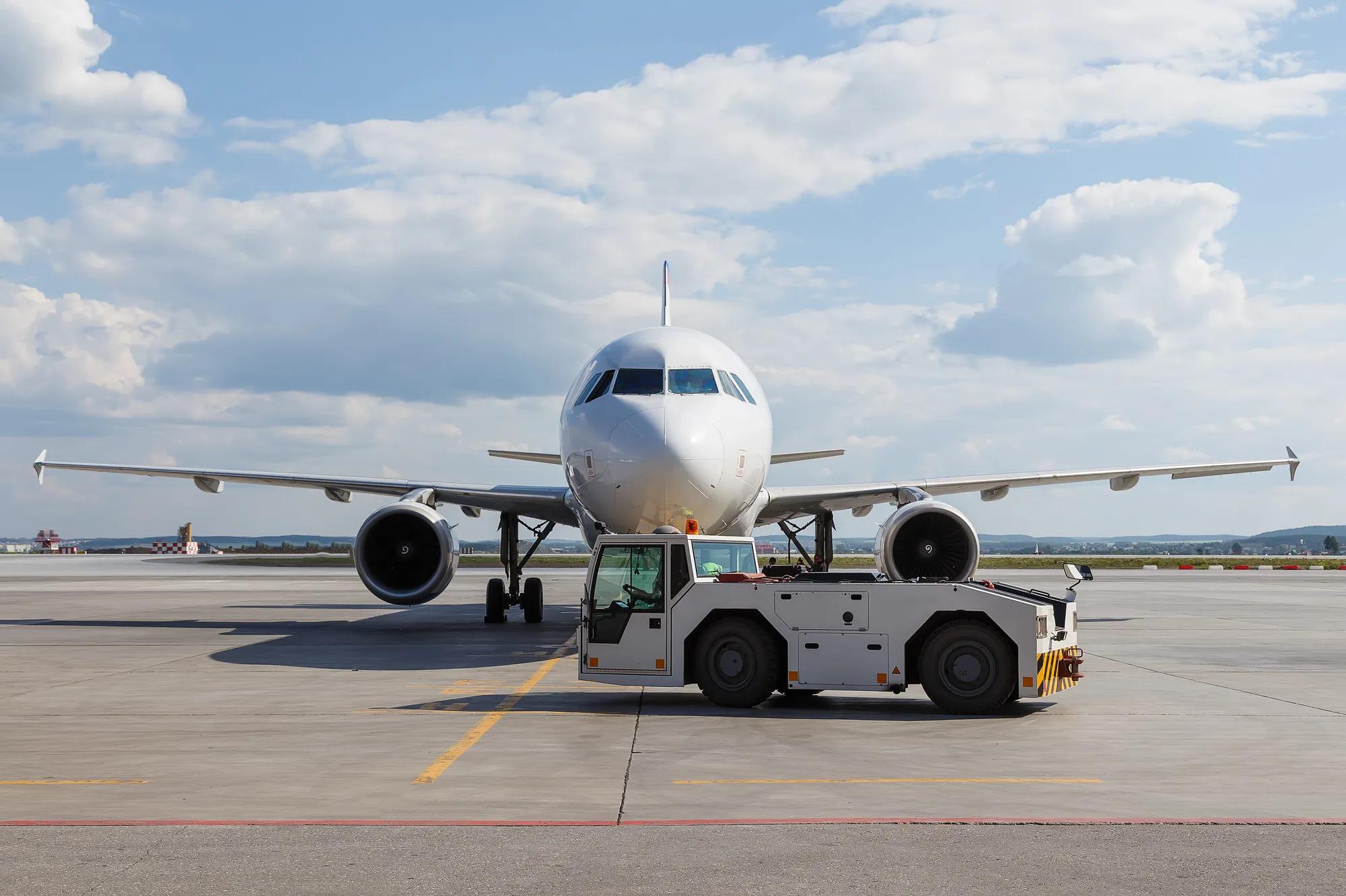 Vehicles towing white modern aircraft on the parking lot