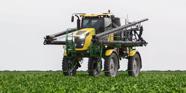 A green and yellow agriculture sprayer is operating in the middle of field of soybeans.