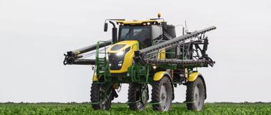 A green and yellow agriculture sprayer is operating in the middle of field of soybeans.