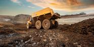 A yellow Volvo mining truck drives in the dirt around a quarry mining site.